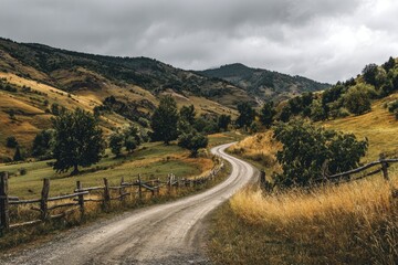 A winding dirt road cuts through golden hills under a cloudy sky, bordered by a rustic fence