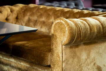 Close-up of a luxurious gold velvet tufted sofa armrest and seat cushion, with a modern black table...