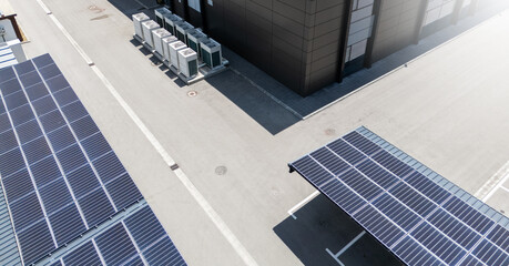 Aerial view of building with solar panels on a roof and parking space with solar canopies