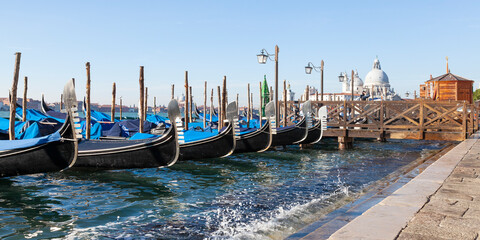 Row of gondolas moored in Bacino San Marco at Acqua Alta high tide with focus to the prows or Fero da Prora, Venice, Veneto, Italy, panorama banner © gozzoli