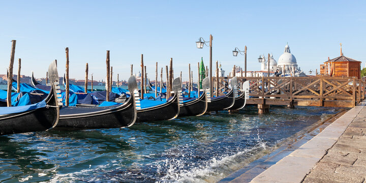 Row of gondolas moored in Bacino San Marco at Acqua Alta high tide with focus to the prows or Fero da Prora, Venice, Veneto, Italy, panorama banner