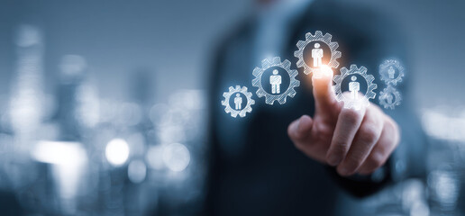 Businessman touching virtual screen with gears and human icons, representing technology and innovation in management. scene conveys sense of progress and connectivity