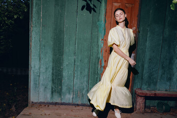 Portrait of a woman model in a flowing yellow dress stands by a weathered doorway in an outdoor...