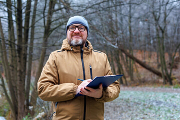 Middle aged ecologist taking notes in a snowy winter forest. Field work, data collection, and nature research on cold season wildlife. Conservation and ecosystem study.