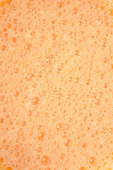 An abstract, full-frame close-up of a vibrant orange, foamy mixture composed of many small bubbles