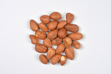A small, scattered pile of shelled, skin-on hazelnuts is centered on a plain, light gray background