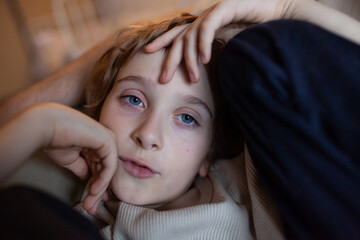 Portrait of 8-year-old caucasian boy with brown hair and blue eyes with thoughtful expression.  Relaxed child resting with hands on head. Soft warm light, calm intimate atmosphere, quiet candid moment