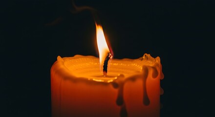 Close-up of a lit candle, with a bright flame, melting wax, and a dark background