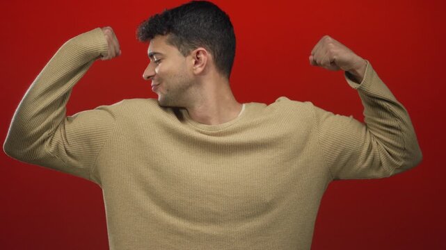 Man lifts biceps to flex against a background while capturing young hispanic energy in red, framing a guy highlighting peak muscle in a studio.