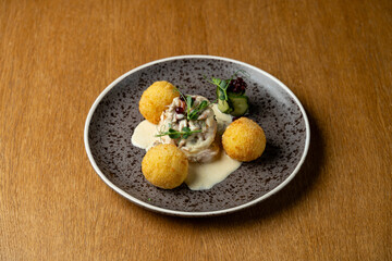 A plate showcases a beautiful arrangement featuring creamy chicken topped with fresh herbs, accompanied by golden croquettes and a drizzle of smooth sauce