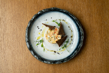 A beautiful dish features vibrant ingredients arranged on a plate. The artistic presentation includes dark bread pieces and green garnishes, set on a wooden table