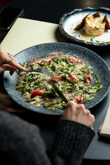 A person savors a vibrant salad filled with fresh greens and cherry tomatoes. Nearby, a dish of creamy dessert waits patiently on the table in a relaxed dining space