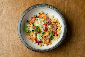 Colorful salad features succulent shrimp, crunchy croutons, and fresh greens, all beautifully arranged in a rustic bowl on a wooden table, showcasing a delightful culinary creation