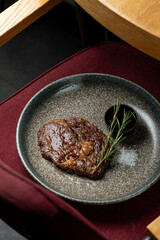 A beautifully cooked steak rests on a elegant plate, accompanied by dark sauce and fresh herbs, inviting diners to enjoy a delightful meal in a warm setting