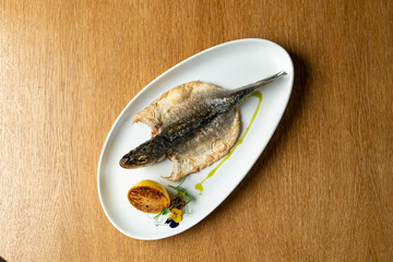 A beautifully cooked grilled fish sits on a white plate, accompanied by a charred lemon and colorful garnish. Perfectly arranged, this dish invites a delightful dining experience