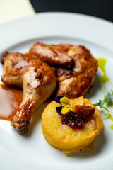 Tender roasted chicken glistens with savory sauce, accompanied by a perfectly cooked potato dish garnished with fruit and herbs on an elegant plate