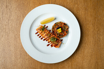 A beautifully plated salmon fillet rests on a clean white dish, garnished with a vibrant vegetable medley. A lemon wedge adds a zesty touch, enhancing the flavorful meal