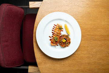 A beautifully arranged plate showcases a succulent piece of fish with vibrant garnishes and a side of colorful vegetables. The warm wooden table adds a welcoming touch