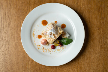 A beautifully arranged dessert features a textured cake topped with powdered sugar, surrounded by colorful fruits and delicate sweets, inviting indulgence in a luxurious setting