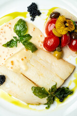 A beautifully arranged plate features tender white fish, vibrant cherry tomatoes, olives, and delicate garnishes, all drizzled with fragrant olive oil. A feast for the eyes and palate awaits