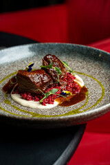 A delicious plate features tender braised beef on vibrant red quinoa, all drizzled with a rich sauce and adorned with fresh greens. The inviting ambiance enhances the dining experience