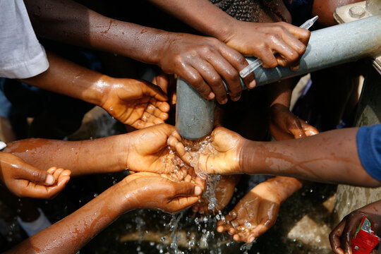 School with a biro pen and children's hands and water drops splashing beneath a running water tap in a West African village as they drink the clean water from a bore hole - Powered by Adobe