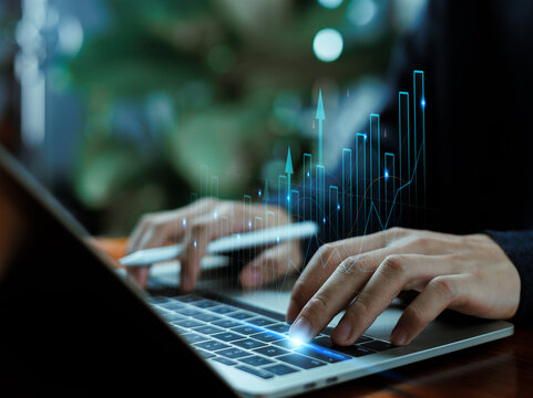 Hands typing on a laptop with rising digital charts and glowing analytics, symbolizing financial growth, data analysis, market trends, business performance, and modern technology.