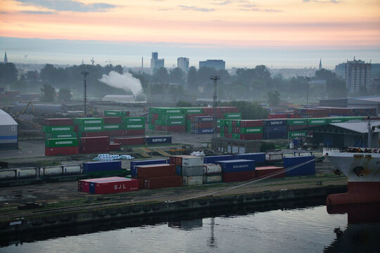 Blick auf Container von Evergreen, Samskip, SJL und Stalogistic am fr&uuml;hen Morgen im Frachthafen von Riga in Lettland mit Skyline der Stadt im Hintergrund