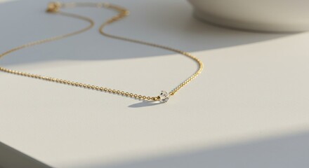 Elegant gold necklace with a single diamond pendant minimalist design on a white surface with soft light and shadow
