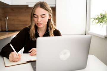 Business woman or female student writing on notebook planner and using laptop computer in the kitchen at home. planning, online working