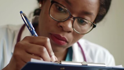 Close-up of a female healthcare professional wearing glasses, diligently writing on a clipboard with a pen - Powered by Adobe