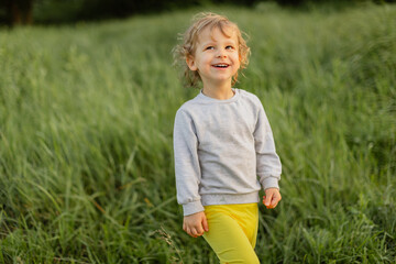 Smiling toddler walking through tall green grass on a sunny day. Natural candid moment with warm light, cheerful expression and relaxed outdoor atmosphere.