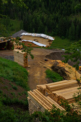 Stacks of processed lumber on a muddy construction site in a rural mountain area.