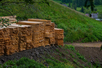 Stack of wooden planks stored outdoors on a hillside near a rural construction site