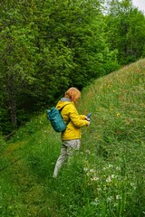 Woman exploring wild grass and flowers on a mountain trail, wearing a yellow jacket and backpack during a summer hike.