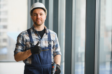Construction worker gesturing thumbs up holding cordless drill in building under construction