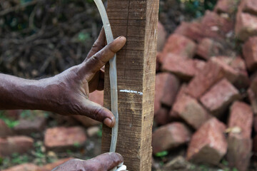 A close-up image showing a person holding and measuring a vertical wooden plank at a construction site
