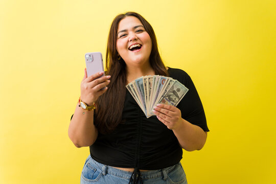 Smiling woman holding phone and cash winning money