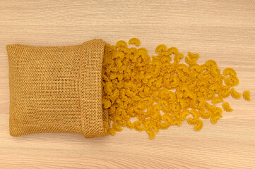 Dry pasta in a canvas bag on a wooden background. Top view.