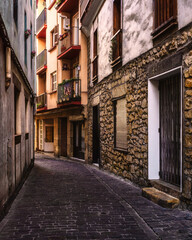 Fototapeta premium Picturesque narrow European street with colorful balconies, stone facades and warm light. Traditional old town alley with a pedestrian walking away