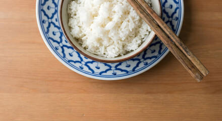 Steamed white rice bowl with chopsticks on Thai patterned plate.
