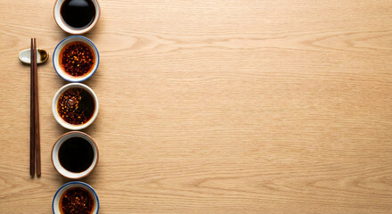 Asian dipping sauces and chopsticks on light wood background copy space.