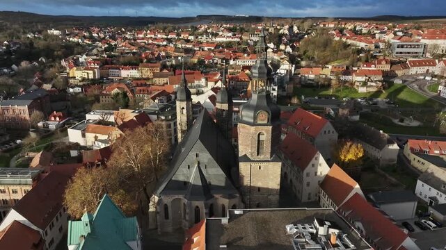 Drone approach to St. Andreas Church in Luther City Eisleben, dramatic pre-storm sky, sunset lighting warms historic houses in Saxony-Anhalt.