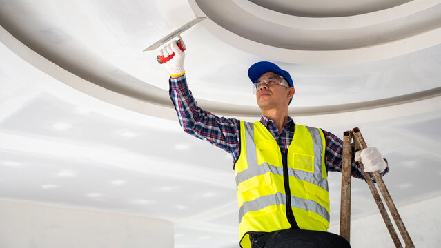 Construction worker applying finishing touches to ceiling interior renovation modern workspace elevated view professional skill application