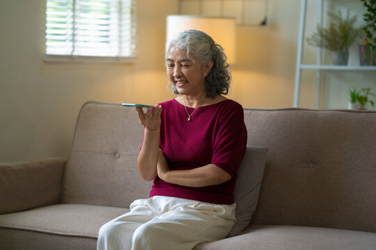 senior woman speaks to smartphone AI voice assistant in her home