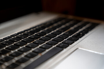 Close-up view of a laptop keyboard showcasing black keys on a silver frame. Captured in warm lighting, ideal for technology or workspace themes.