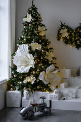 Elegant Christmas tree decorated with huge white flowers and gifts, featuring a vintage toy race car.