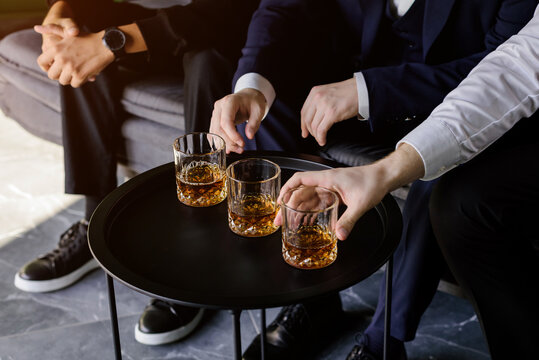 Business colleagues in suits sharing whiskey glasses on a modern black table during a corporate event or negotiation.