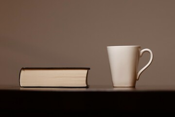One book with a white cup, on a dark table, view straight ahead