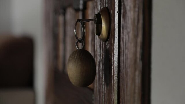 A close-up of wooden doors with a key inserted, featuring a wooden keychain gently swaying in the wind a key to a hotel room in the mountains.
